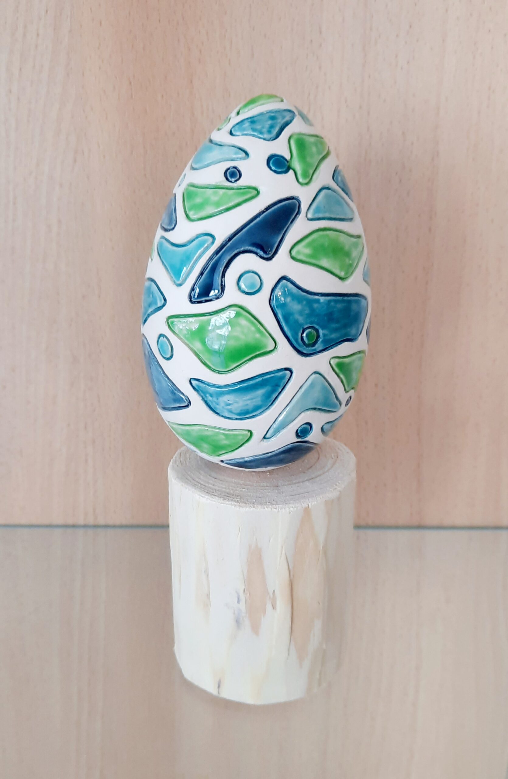 Œuf décoratif en céramique bleu et vert posé sur un support en bois flotté