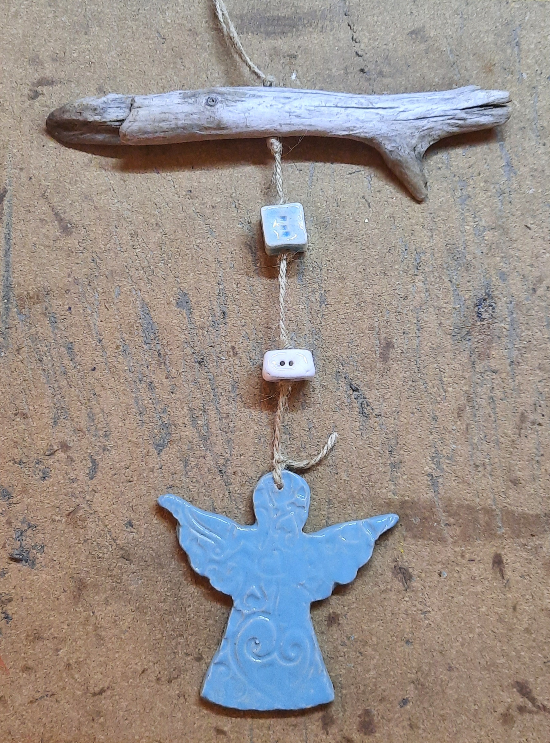 Suspension décorative avec ange bleu en céramique sous une branche en bois flotté